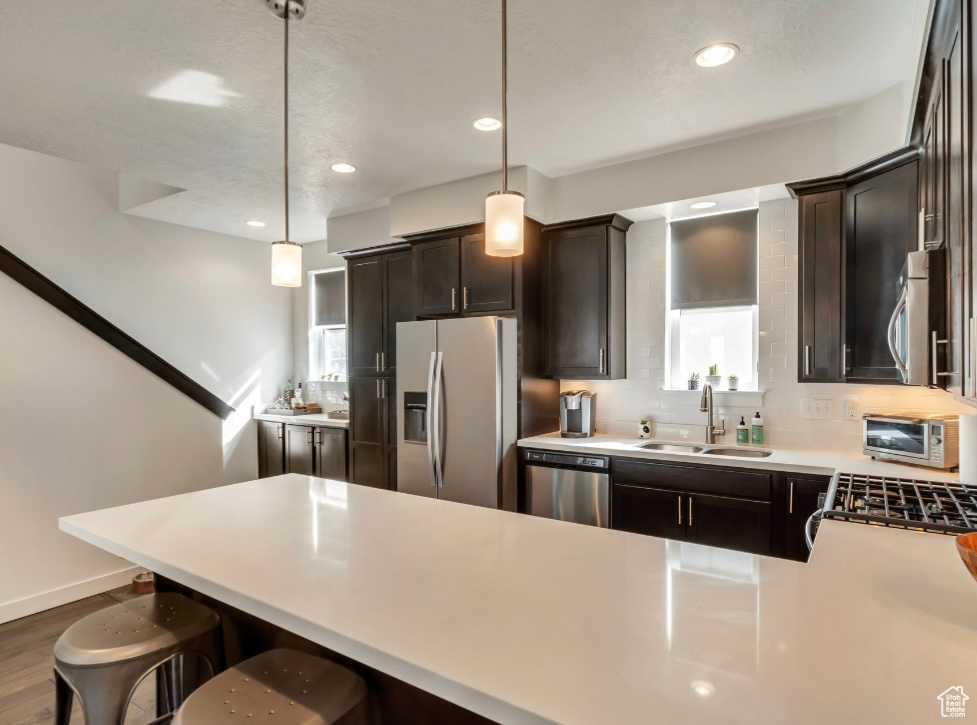 Kitchen featuring stainless steel appliances, tasteful backsplash, a breakfast bar, dark brown cabinets, and light countertops