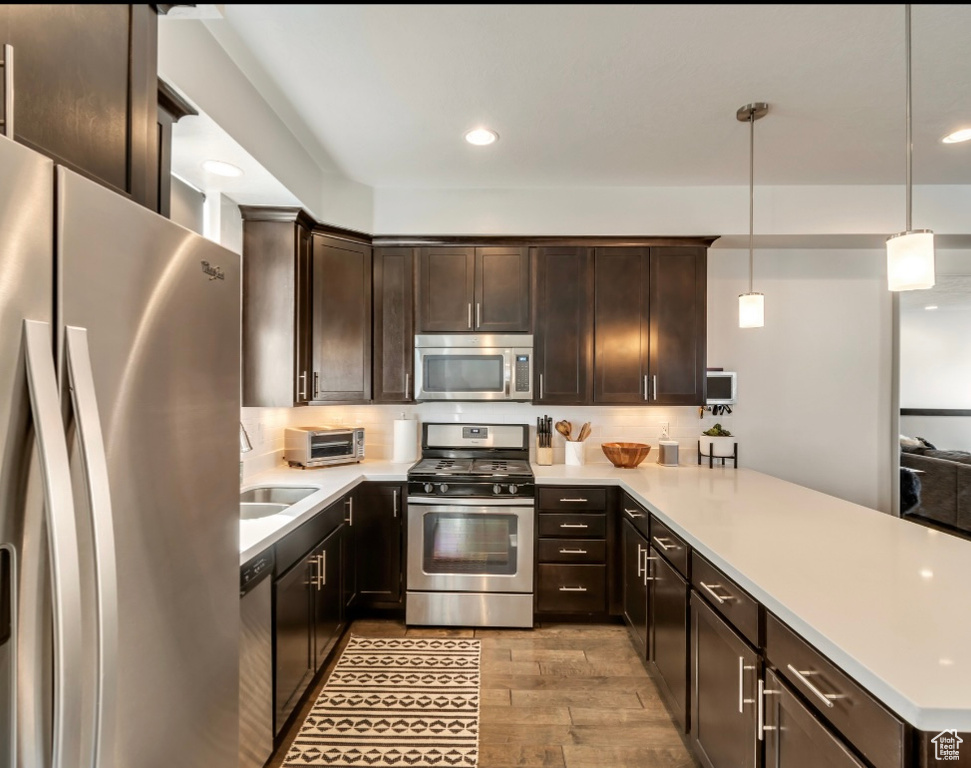 Kitchen with appliances with stainless steel finishes, a peninsula, dark brown cabinetry, light wood-style flooring, and light countertops
