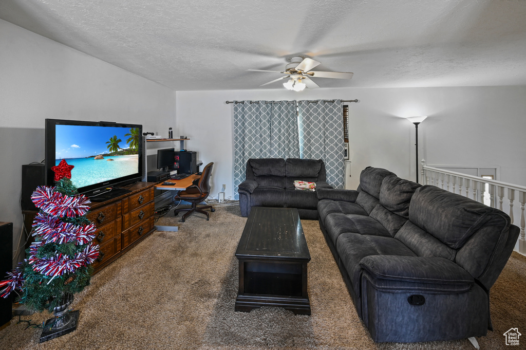 Carpeted living room featuring a ceiling fan, a textured ceiling, and an office area