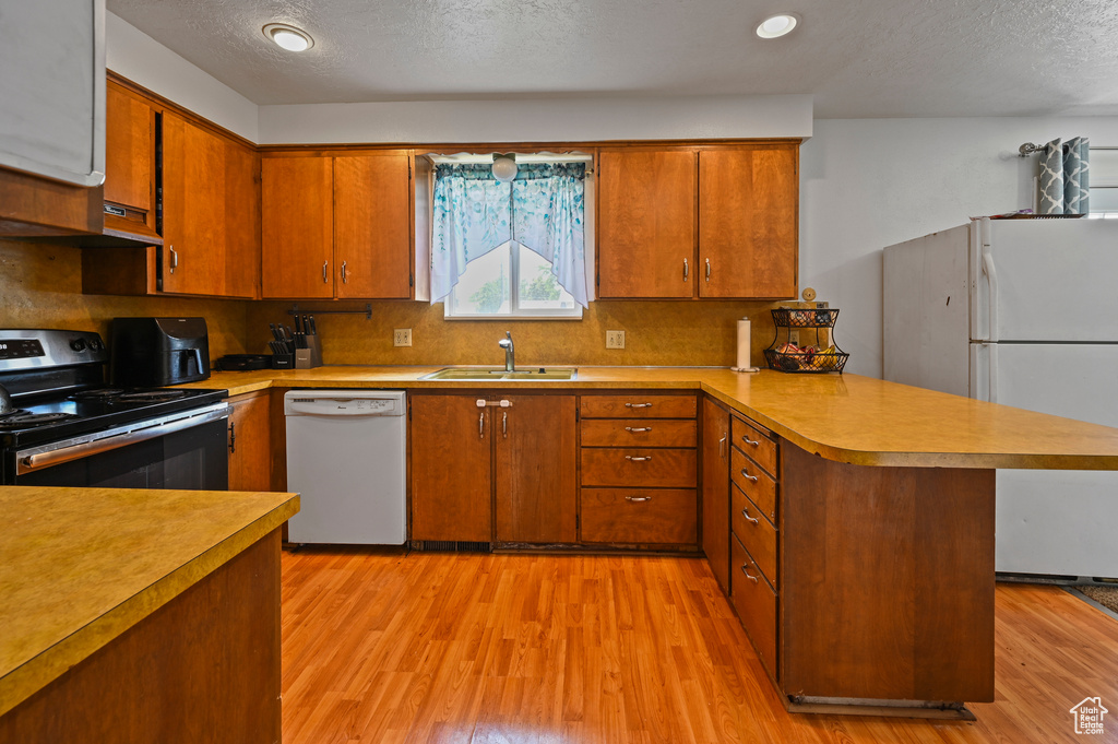 Kitchen with white appliances, a peninsula, light wood-type flooring, light countertops, and backsplash