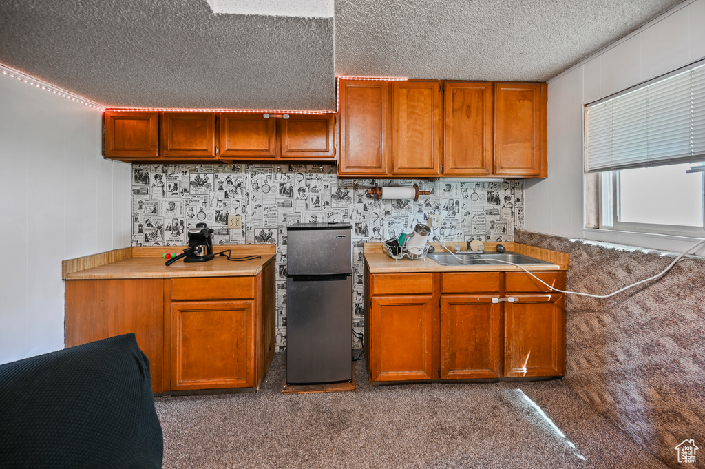 Kitchen with freestanding refrigerator, a textured ceiling, brown cabinets, and light countertops