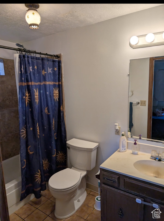 Bathroom featuring tile patterned flooring, vanity, shower / bath combo with shower curtain, and a textured ceiling