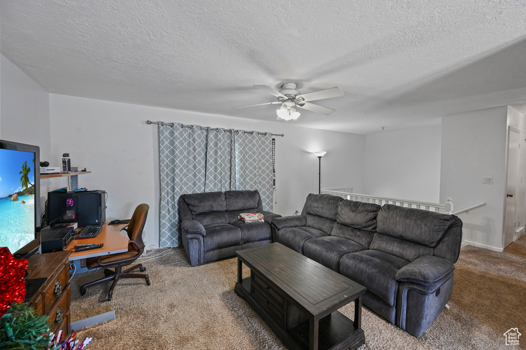Carpeted living area with ceiling fan, a desk, and a textured ceiling