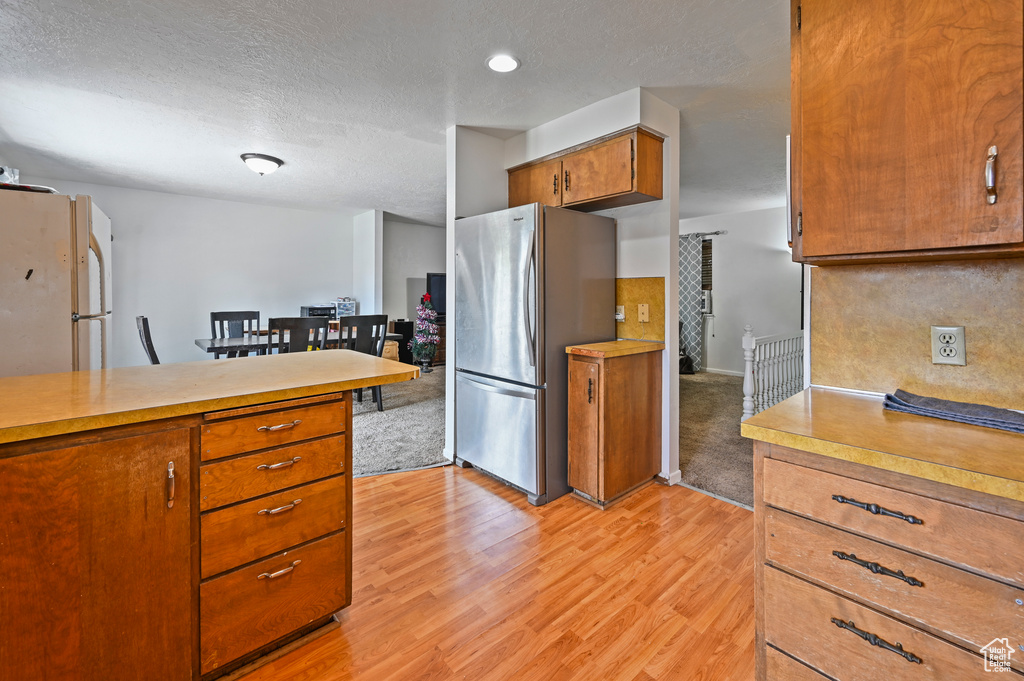 Kitchen with freestanding refrigerator, light countertops, brown cabinets, light wood-style floors, and a textured ceiling
