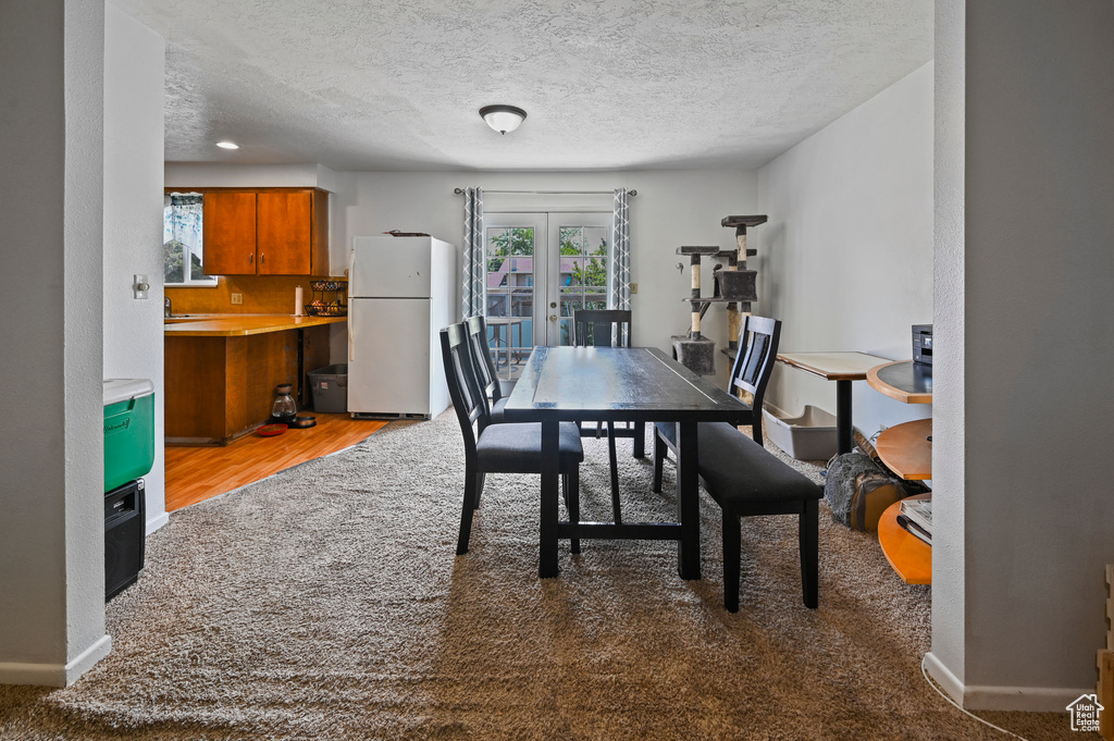 Carpeted dining space with a textured ceiling, french doors, and wood finished floors