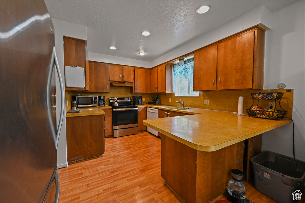 Kitchen with stainless steel appliances, a peninsula, under cabinet range hood, light wood-type flooring, and light countertops