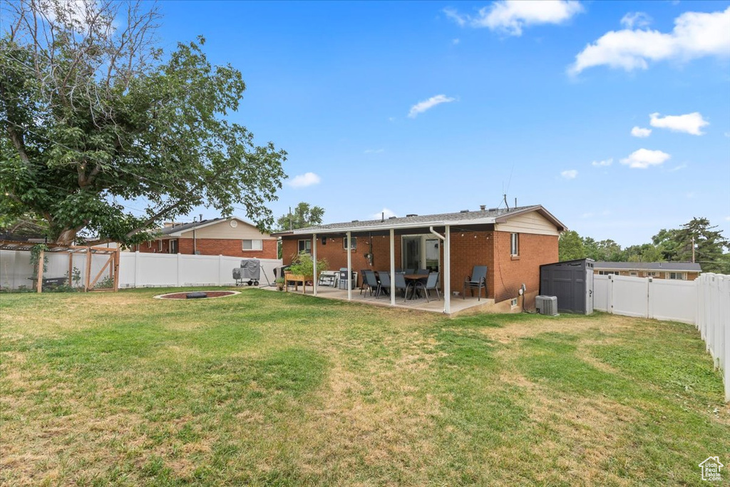 Back of house featuring brick siding, a patio, a fenced backyard, and a storage unit