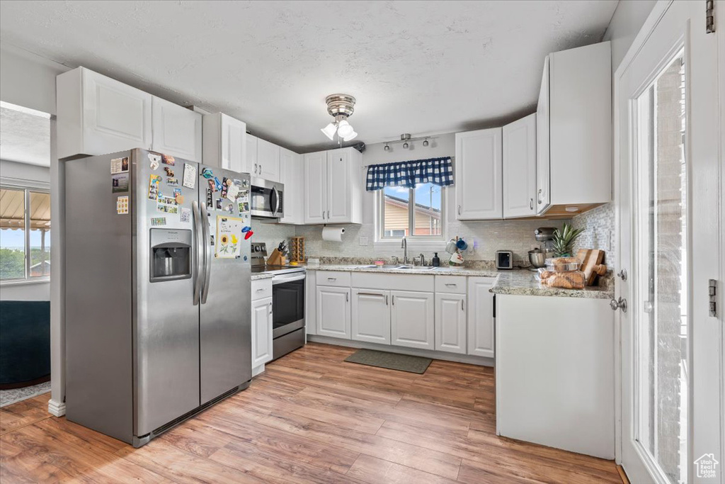 Kitchen with appliances with stainless steel finishes, light wood-type flooring, tasteful backsplash, white cabinets, and a textured ceiling