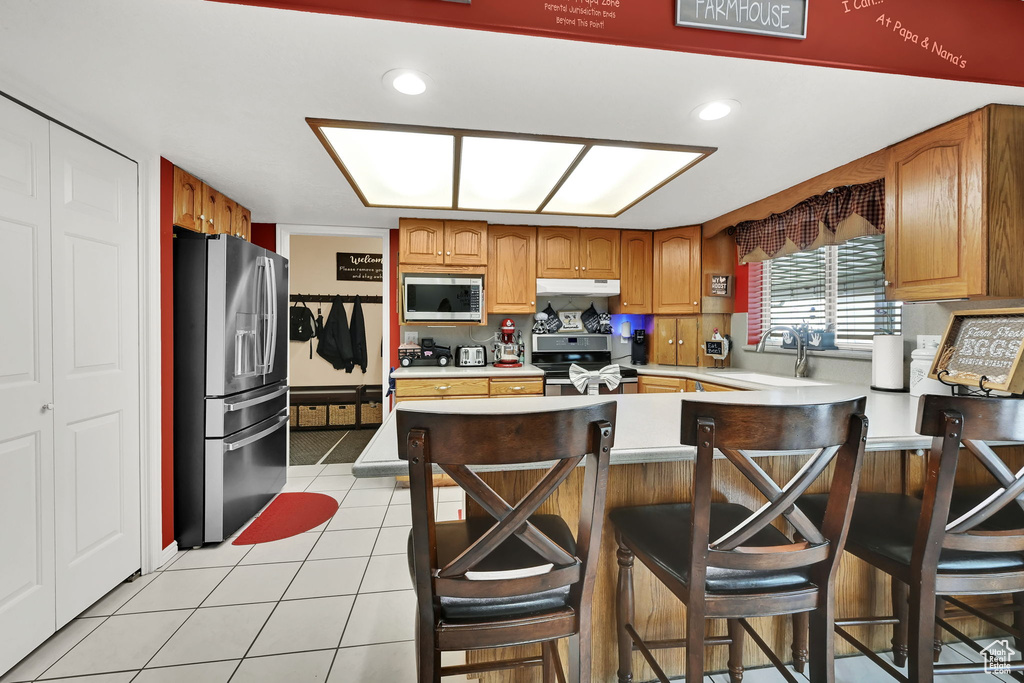 Kitchen with stainless steel appliances, a peninsula, light countertops, light tile patterned flooring, and under cabinet range hood
