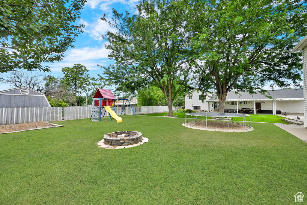 Fenced backyard with a trampoline, a playground, an outdoor fire pit, and a shed