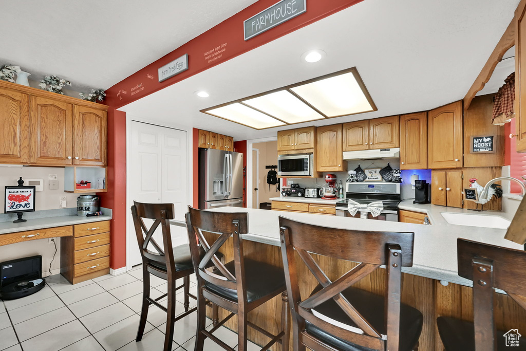 Kitchen featuring stainless steel appliances, under cabinet range hood, light countertops, built in desk, and a peninsula