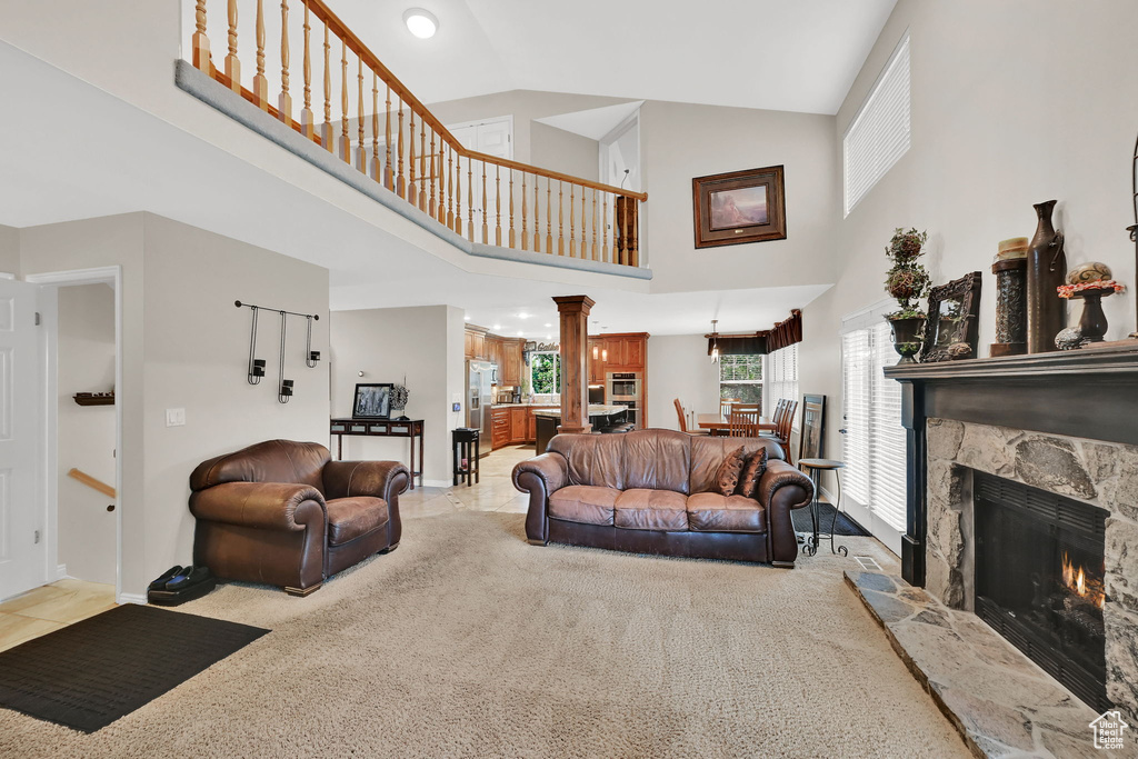 Living area featuring a stone fireplace, high vaulted ceiling, carpet floors, and ornate columns