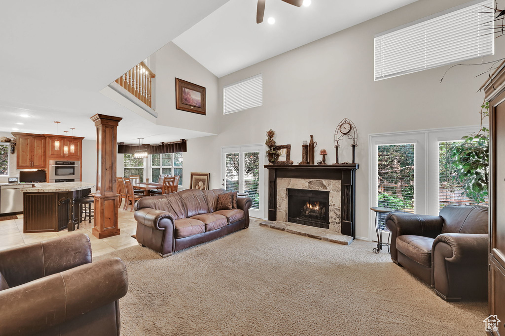 Living room featuring a towering ceiling, ornate columns, a ceiling fan, a fireplace, and light carpet