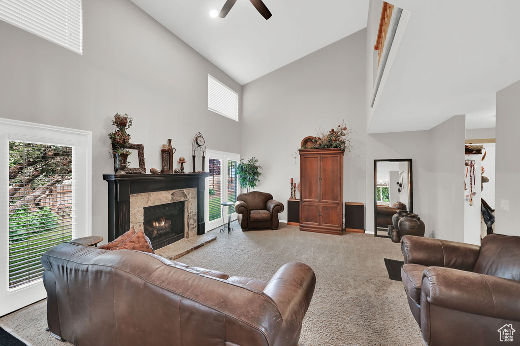 Carpeted living room with high vaulted ceiling, a ceiling fan, a warm lit fireplace, and healthy amount of natural light