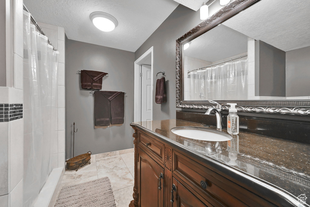 Full bath featuring a textured ceiling, vanity, a shower with shower curtain, and marble look tiles