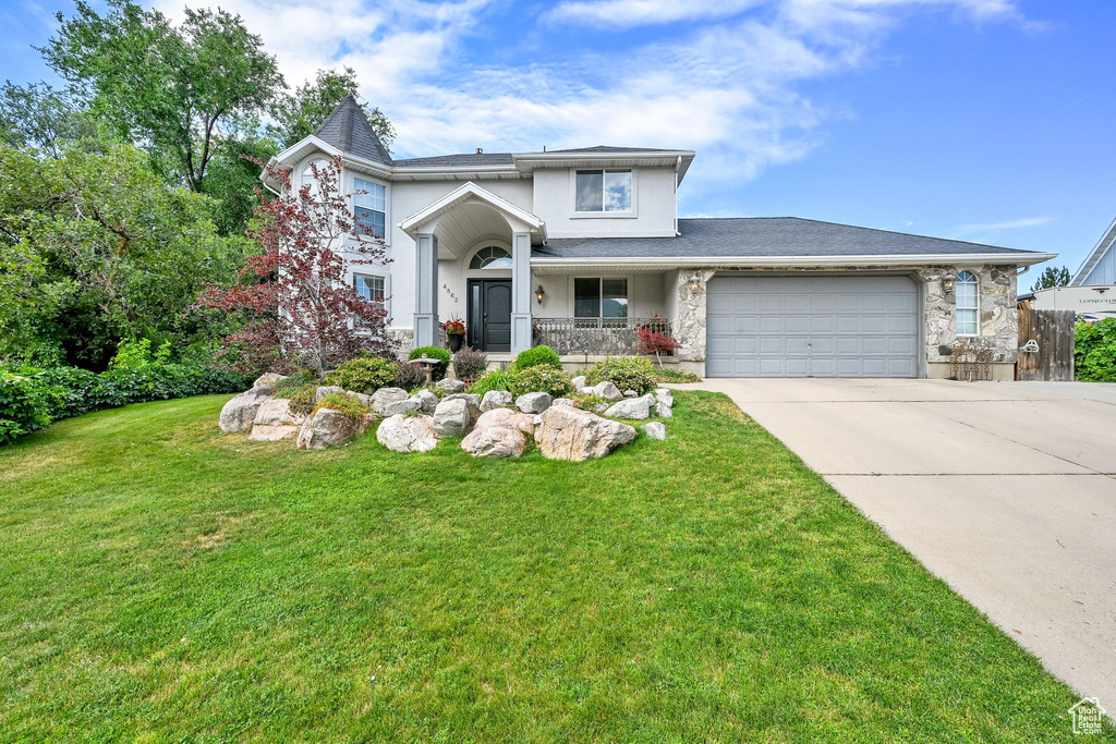 Traditional-style house featuring concrete driveway, a garage, stucco siding, a front lawn, and stone siding