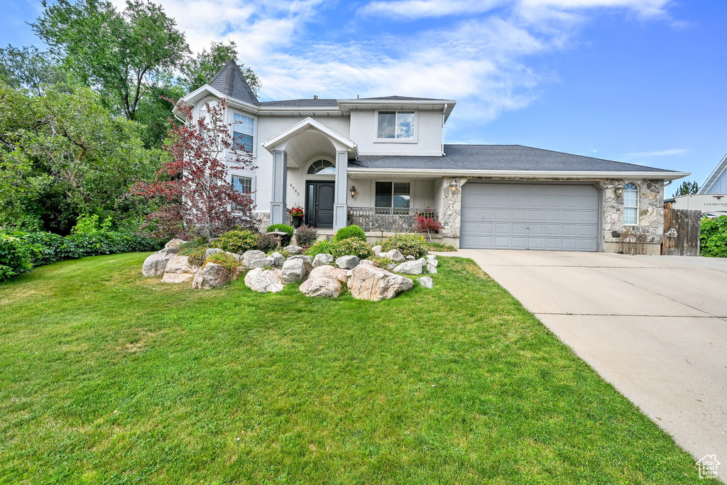 View of front of property with stucco siding, a garage, driveway, a front lawn, and stone siding