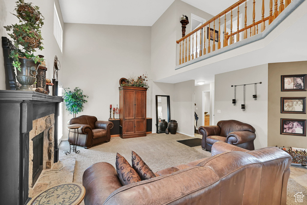 Living room featuring a high ceiling, light colored carpet, and a stone fireplace