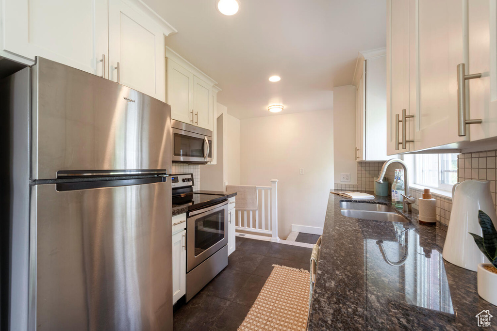 Kitchen featuring stainless steel appliances, tasteful backsplash, dark stone countertops, white cabinets, and recessed lighting