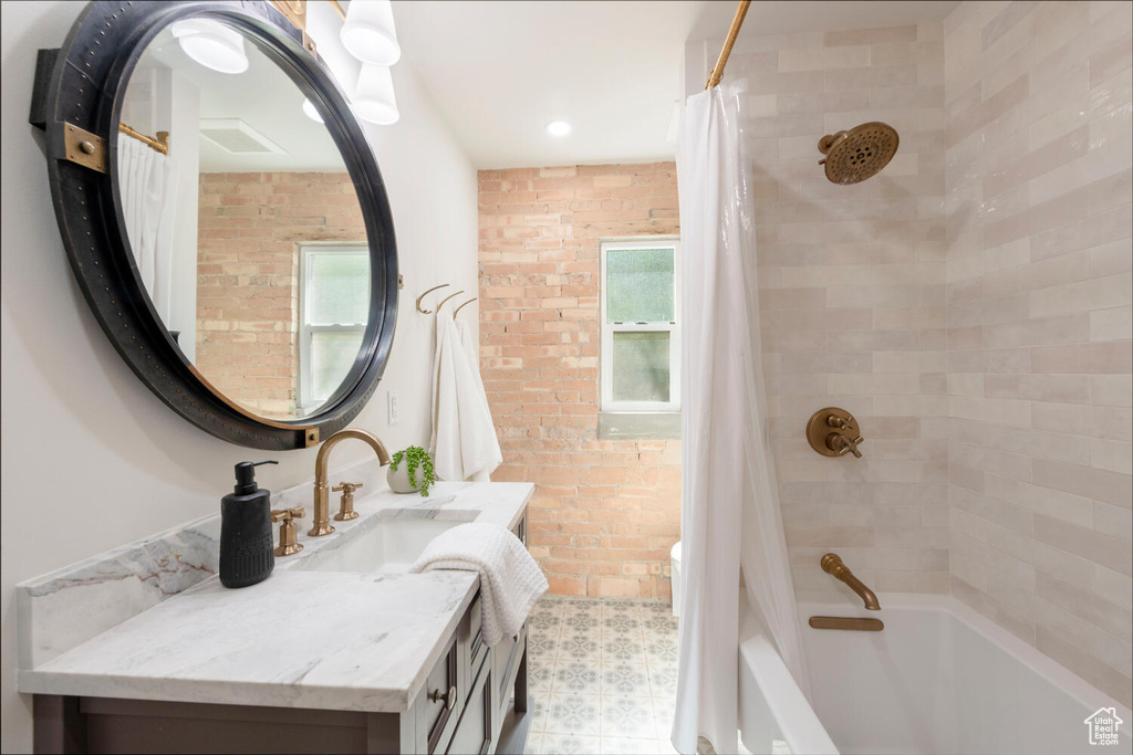 Bathroom featuring vanity, shower / bath combination with curtain, brick wall, and healthy amount of natural light