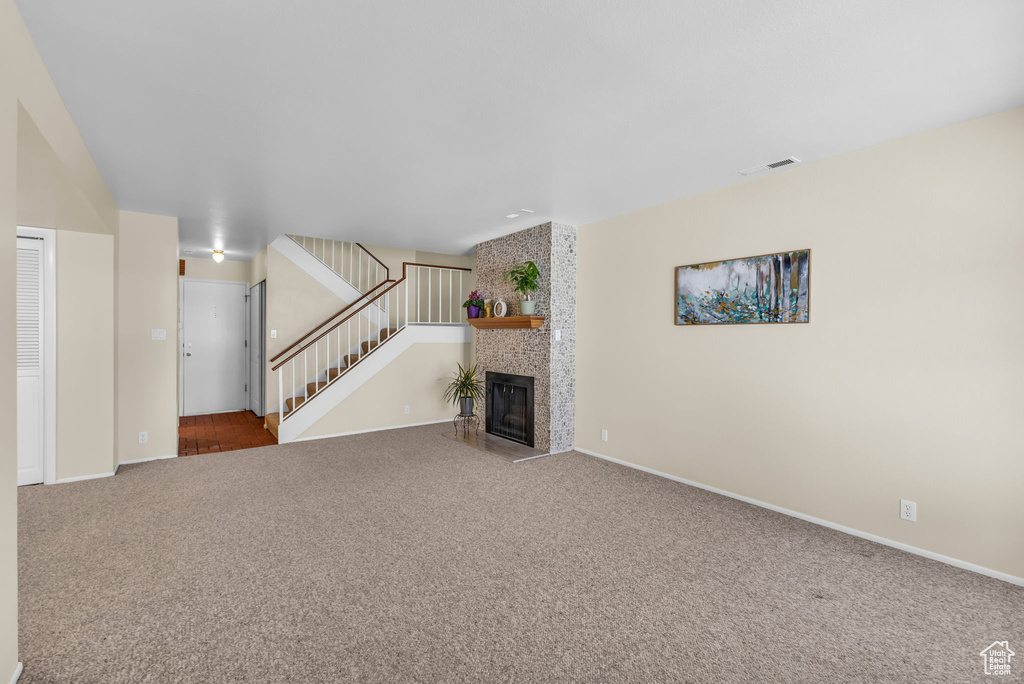 Unfurnished living room featuring carpet, stairway, and a fireplace
