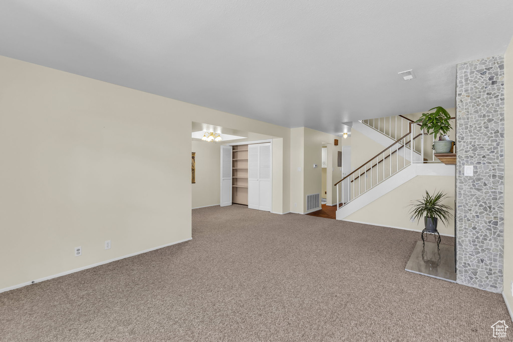Unfurnished living room featuring carpet flooring and stairway