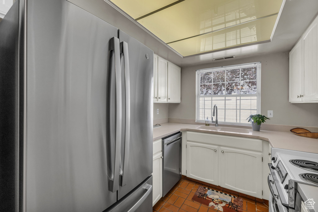 Kitchen with stainless steel appliances, light countertops, white cabinetry, and brick patterned floors