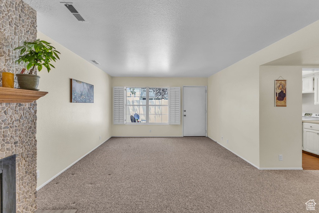 Unfurnished living room featuring carpet floors, a fireplace, and a textured ceiling