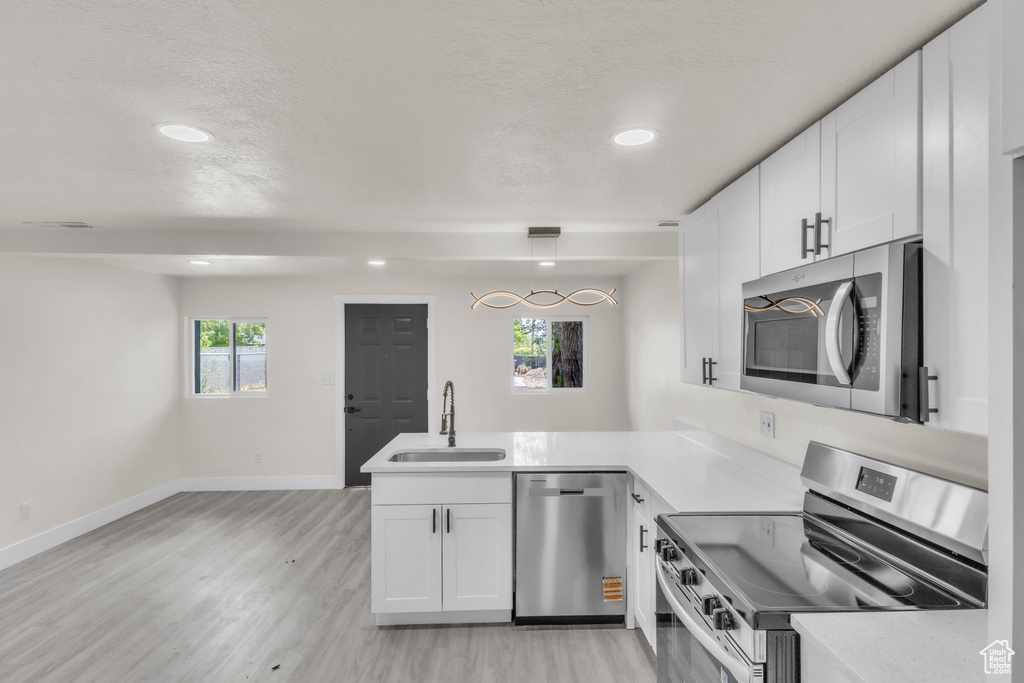 Kitchen with appliances with stainless steel finishes, a peninsula, light wood finished floors, recessed lighting, and white cabinetry