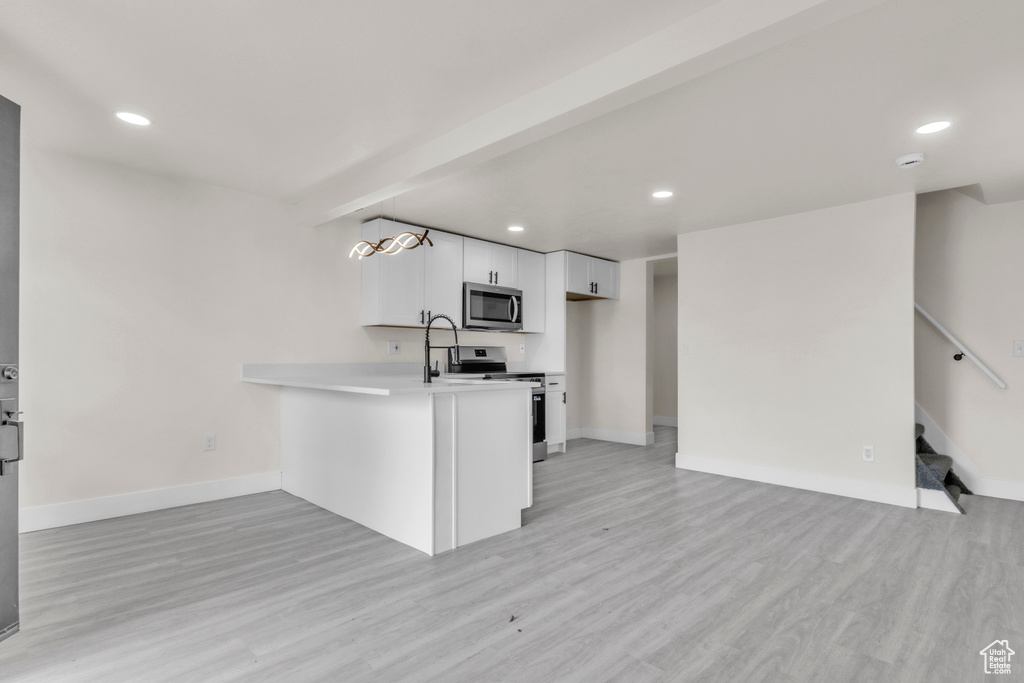 Kitchen with stainless steel appliances, white cabinetry, light countertops, light wood finished floors, and open floor plan