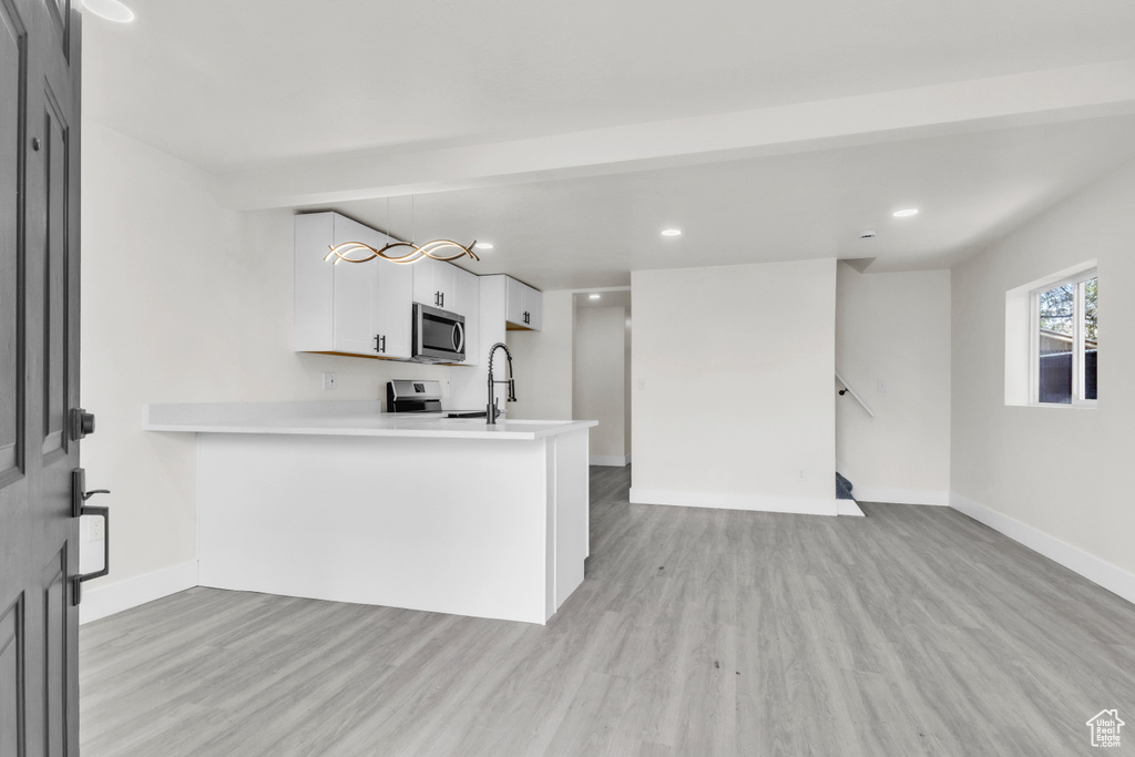 Kitchen with stainless steel microwave, light wood finished floors, light countertops, a peninsula, and recessed lighting
