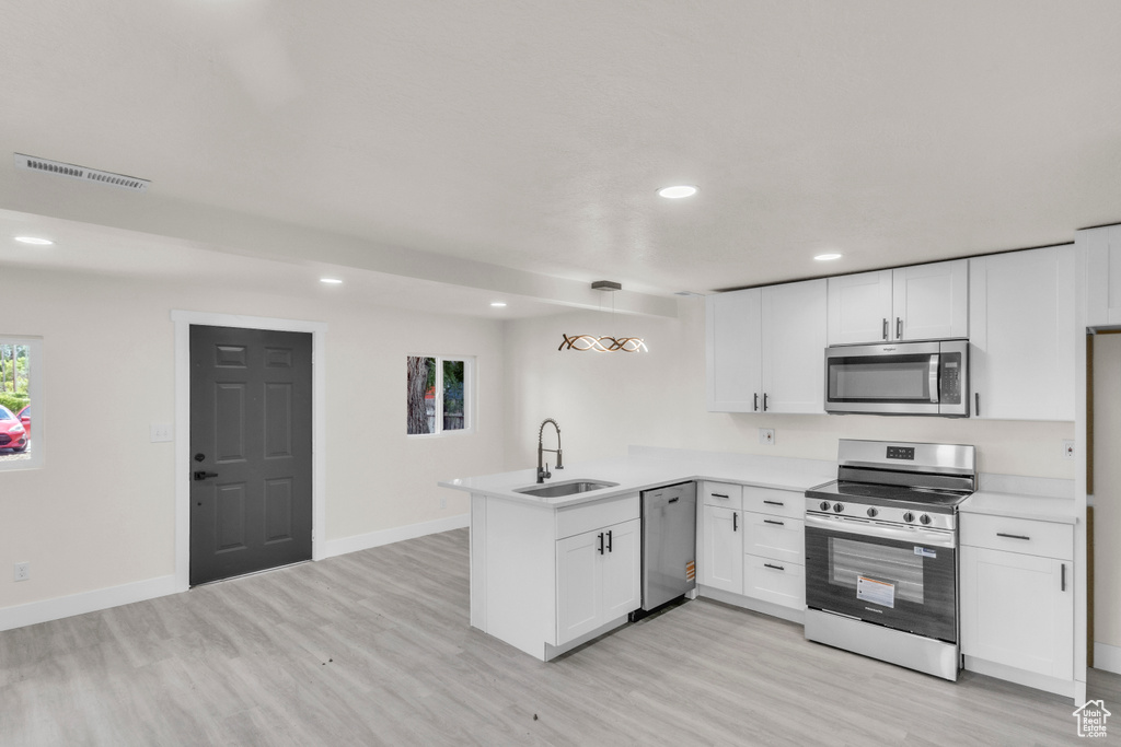 Kitchen featuring appliances with stainless steel finishes, a peninsula, light wood finished floors, recessed lighting, and white cabinets