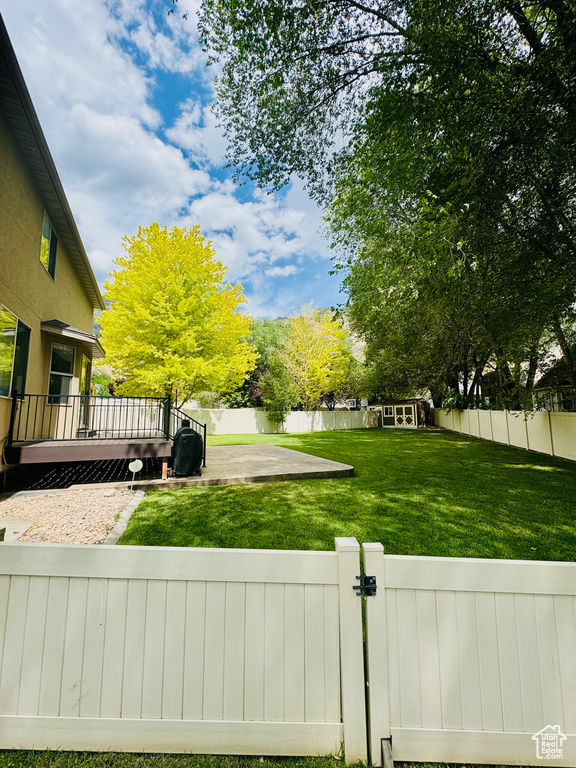 Fenced backyard with a deck, a gate, an outdoor structure, and a patio area
