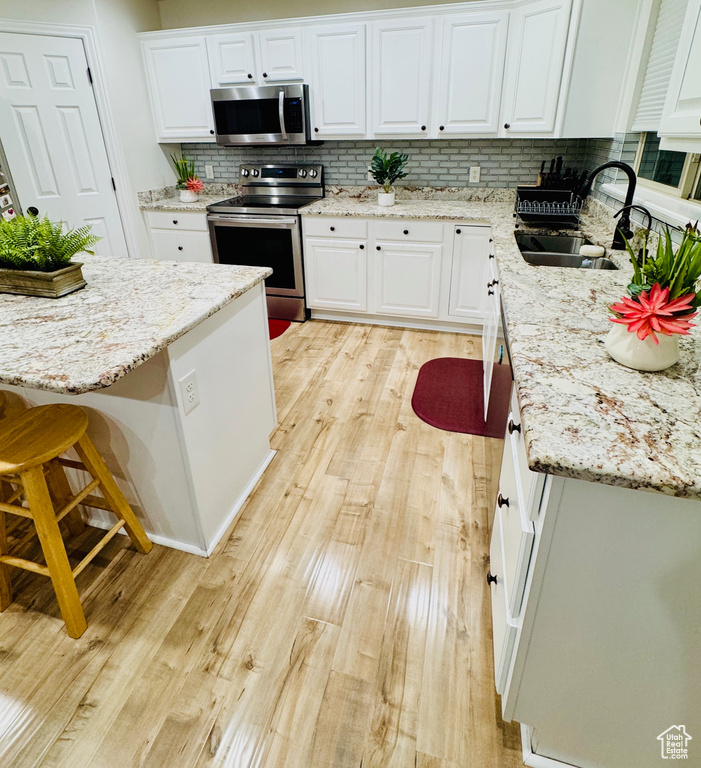 Kitchen featuring stainless steel appliances, tasteful backsplash, light wood-style flooring, and white cabinetry