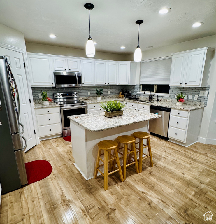 Kitchen featuring stainless steel appliances, tasteful backsplash, light wood-style floors, white cabinetry, and recessed lighting