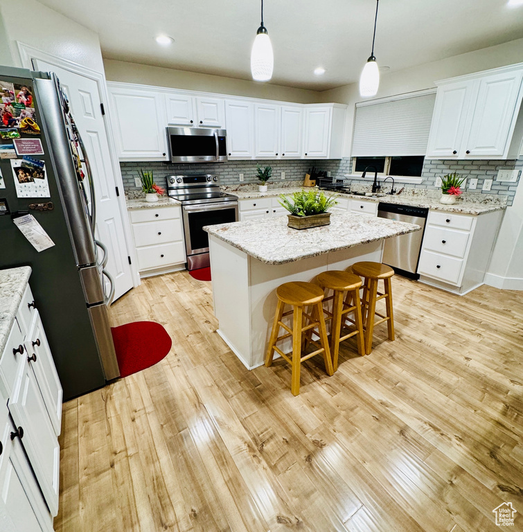 Kitchen with appliances with stainless steel finishes, decorative backsplash, light wood finished floors, white cabinets, and recessed lighting