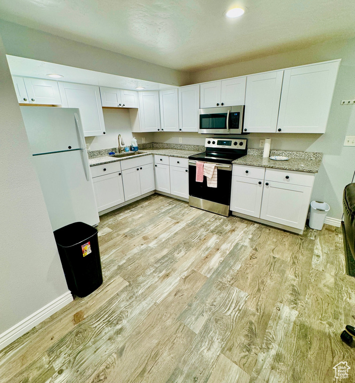 Kitchen with stainless steel appliances, light wood-style floors, white cabinetry, light stone counters, and recessed lighting