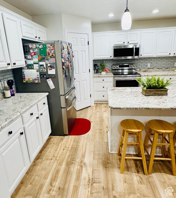 Kitchen featuring appliances with stainless steel finishes, a breakfast bar area, backsplash, light wood finished floors, and recessed lighting