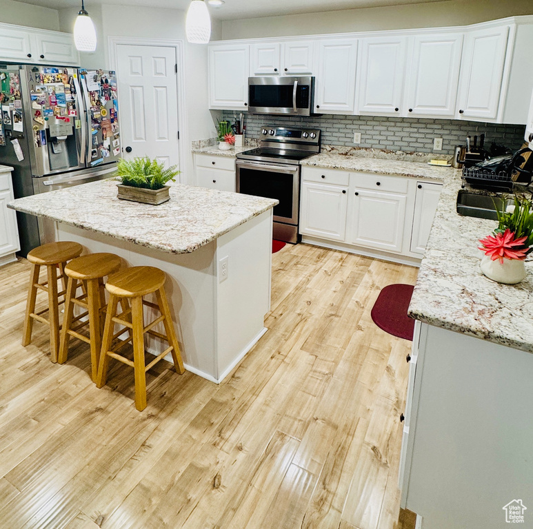 Kitchen with appliances with stainless steel finishes, light wood-type flooring, tasteful backsplash, white cabinetry, and a center island