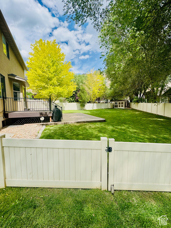 Fenced backyard featuring a wooden deck, an outdoor structure, a gate, and a patio