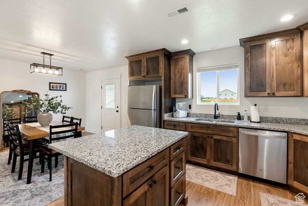 Kitchen featuring appliances with stainless steel finishes, light wood-type flooring, plenty of natural light, and light stone counters