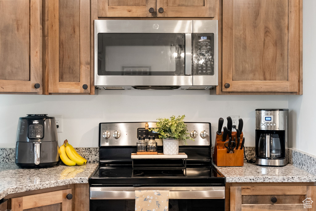 Kitchen with appliances with stainless steel finishes, brown cabinetry, and light stone countertops