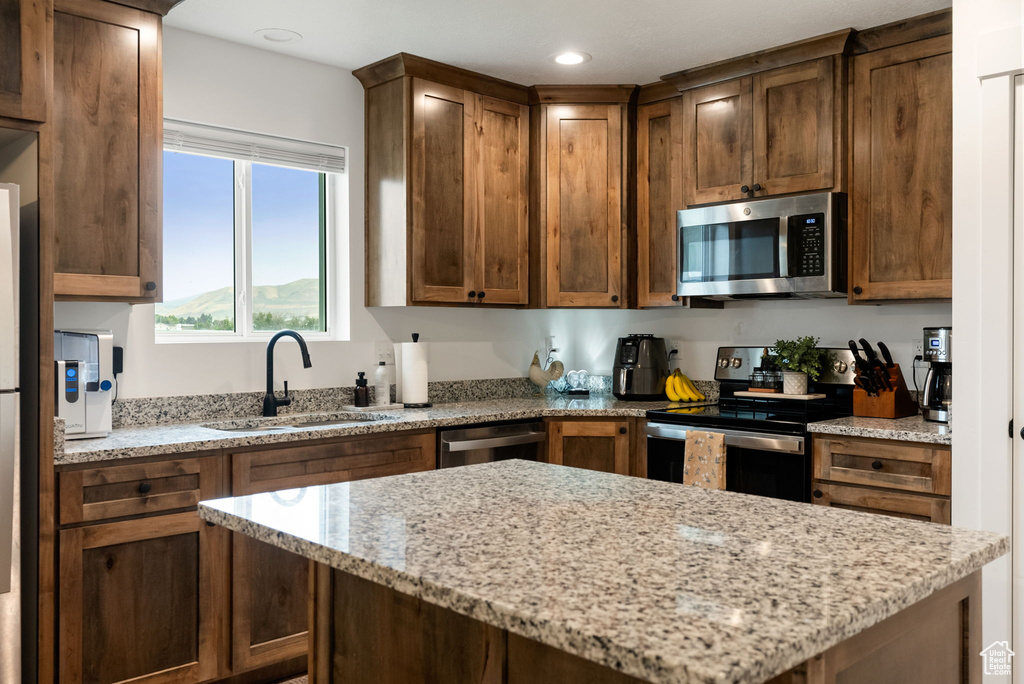 Kitchen featuring appliances with stainless steel finishes, light stone counters, a center island, and recessed lighting