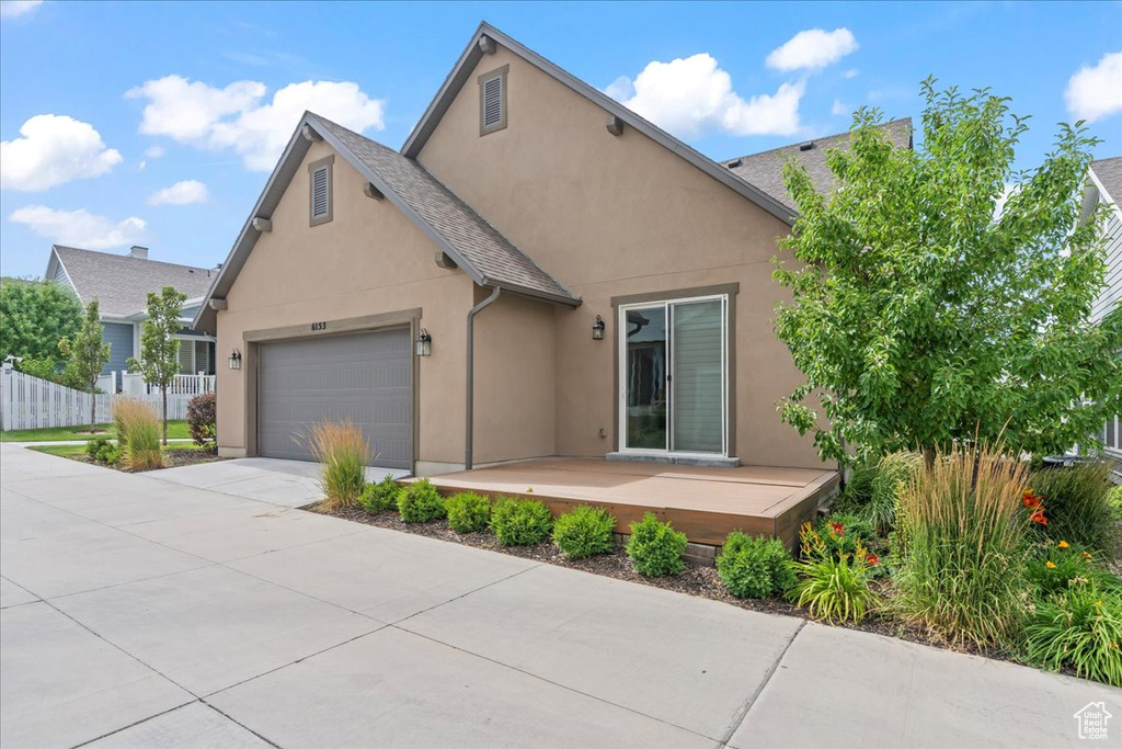 View of front of house with stucco siding, an attached garage, concrete driveway, and a wooden deck