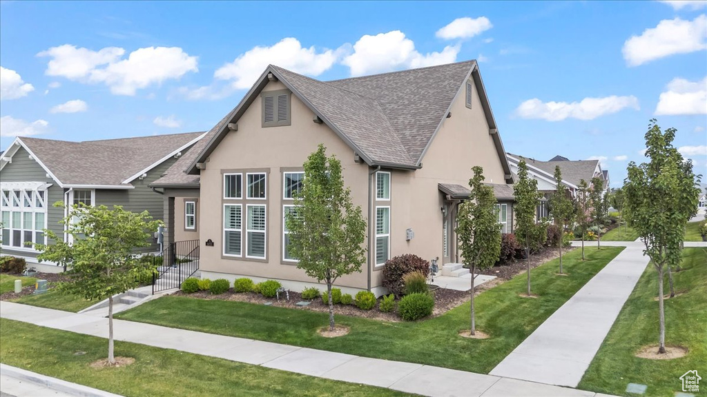 Tudor-style house with stucco siding, a front yard, and a shingled roof