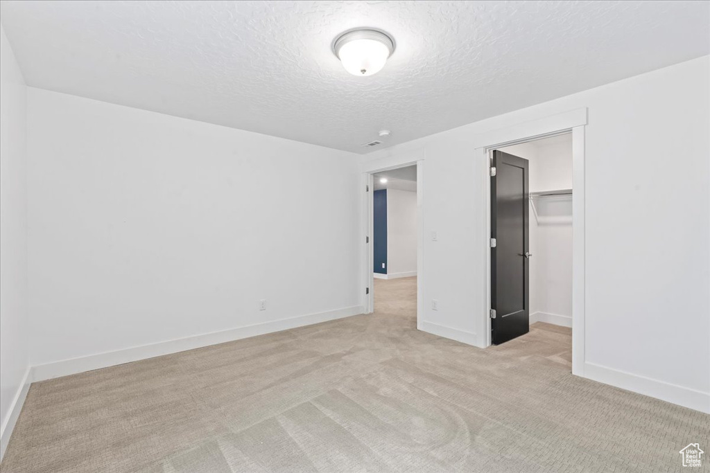 Unfurnished bedroom with a textured ceiling, light colored carpet, a closet, and a walk in closet