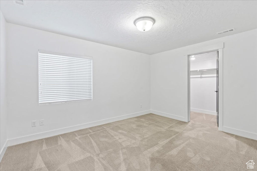 Unfurnished bedroom featuring a textured ceiling, light colored carpet, a spacious closet, and a closet