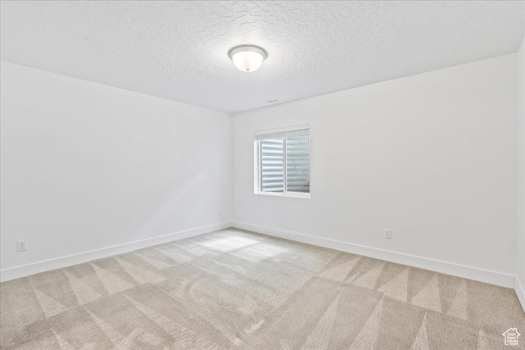 Empty room with light colored carpet and a textured ceiling