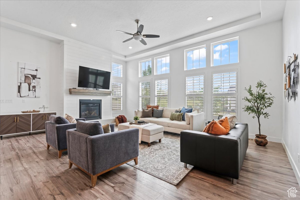 Living room featuring light wood-style floors, ceiling fan, a large fireplace, recessed lighting, and a towering ceiling