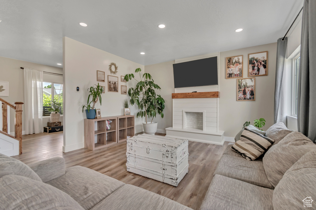 Living room featuring stairway, light wood-type flooring, a fireplace with raised hearth, and recessed lighting